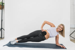 Jess Skipper in a white top and black leggings doing a side plank